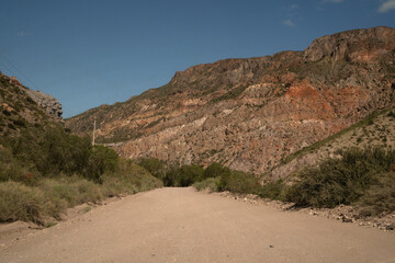Traveling into the desert. View of the dirt road across the arid environment, rock and sandstone mountains.