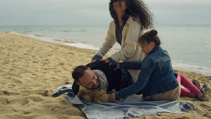 Playful parents child enjoying family vacation on sea beach picnic outdoors.