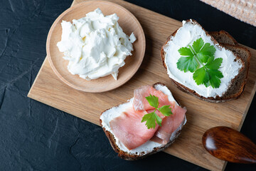 Home made bread on a wooden cutting board with curd cheese and salmon. Decorated with green herbs