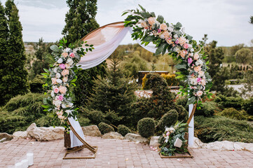 A round wedding arch decorated with colorful flowers and fabric stands in a park, a garden in...