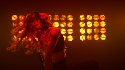 Passionate woman shaking hair performing erotic dance on chair nightclub.