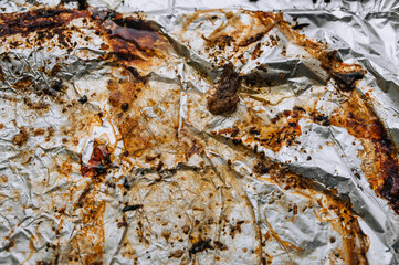 Background, texture, top view of a dirty, greased, sunflower oil, meat dish, colored foil. Photo after cooking.