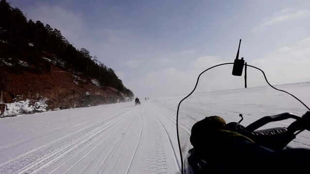 riding snow scooter over snowy and frozen river in sunny winter day, view from driver seat