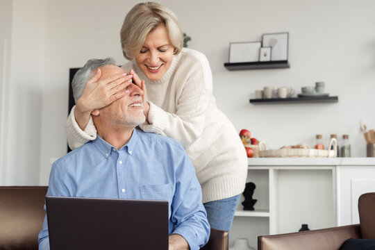 Woman cover husband eyes while he work on laptop - Powered by Adobe