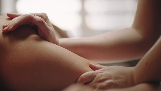 masseuse is massaging arm and back of male patient in chiropractic clinic, closeup view, professional massage