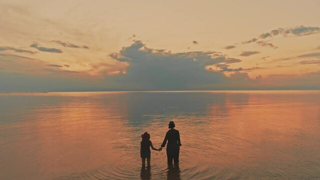Two sisters standing knee deep in the sea looking at the beautiful sunset. Clouds and sky reflecting it the calm water. Delicate ripples.