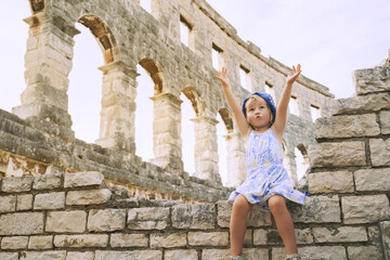 Сute little girl with family exploring Roman Amphitheater Arena like as Coliseum - famous tourist...