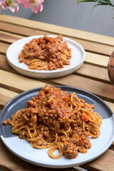 Pasta with meat, tomato sauce, vegetables and grated parmesan cheese. Delicious Italian spaghetti Bolognese served on plate in wooden table