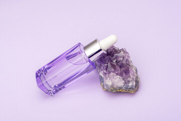Purple cosmetic serum bottle on amethyst crystal stone, close up