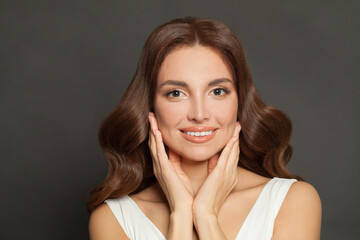 Beautiful woman with perfect clean skin holding her hands near her face on gray background. Facial treatment and skin care concept