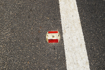 Metal Road stud with Red reflector on asphalt road with white painted lane marking line as divider...