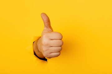 Hand shows a thumb up through a hole of yellow paper wall