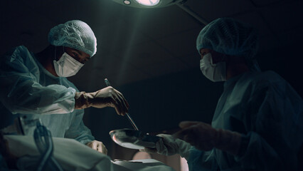 Surgeon operating in dark emergency ward. Medical worker taking bloody tampons.