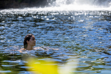 Fototapeta premium A brunette woman refreshes herself by bathing in a river near a big waterfall of the cerrrado biome in west-central Brazil. Leisure. Lifestyle. Life in Nature. Nature journey.