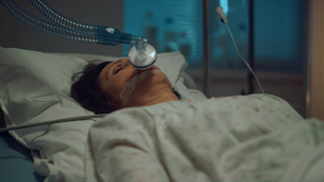 Patient with oxygen mask lying hospital bed in hospital intensive care unit. 