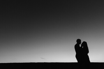  Silhouettes of young couple on the horizon background. Black and white photo