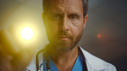 Doctor checking with flashlight test portrait. Serious male healthcare worker. - obrazy, fototapety, plakaty