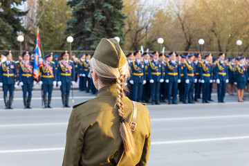 View from behind the back of a woman in a military Soviet uniform on the blurry ranks of military...