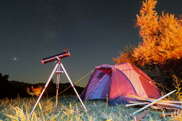 Tourist camping tent and reflector telescope on a tripod at night under starry sky