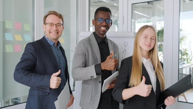 Positive colleagues business partners, diverse team, startup group project. African black man and caucasian man and woman show thumbs up and smile. Ethnic gender diversity, office workers