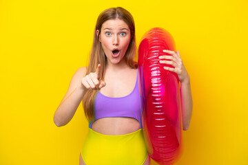 Young caucasian woman holding air mattress isolated on yellow background surprised and pointing...