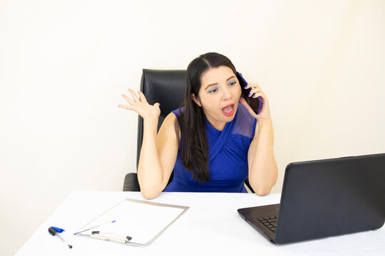 cute successful CEO assistant wearing blue blouse surprised taking call on cellphone, desk with ducuments and laptop, on white background