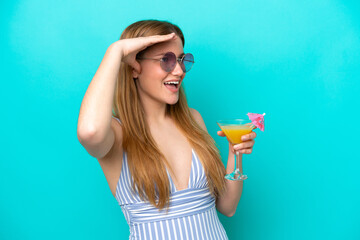 Young woman isolated on blue background in swimsuit and holding a cocktail