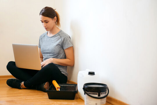 Portrait of young beautiful woman sitting with laptop while painting new apartment