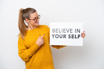 Young caucasian woman isolated on white background holding a placard with text Believe In Your Self and pointing it