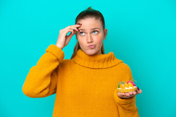 Young caucasian woman holding a tartlet isolated on blue background having doubts and with confuse...