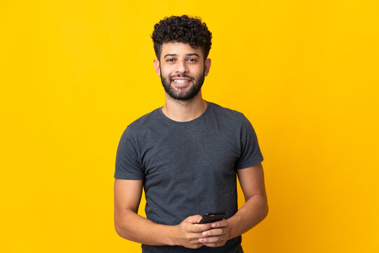 Young Moroccan man isolated on yellow background sending a message with the mobile