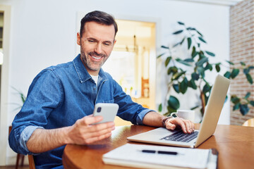 Successful man using smart phone and laptop at home office