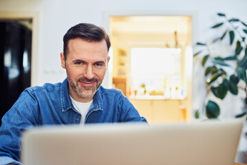 Closeup picture of middle aged man using laptop at home wearing denim shirt
