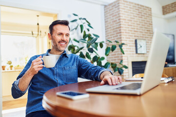 Relaxed casual man working on laptop drinking coffee at home