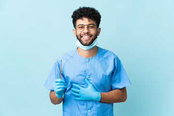 Moroccan dentist man holding tools isolated on blue background smiling a lot