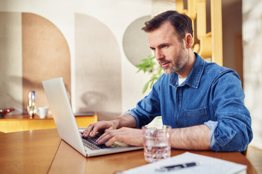 Focused midaged man working on laptop at home