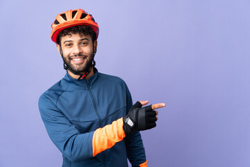 Young Moroccan cyclist man isolated on purple background pointing finger to the side and presenting a product - obrazy, fototapety, plakaty