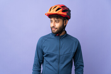 Young Moroccan cyclist man isolated on purple background looking to the side and smiling - obrazy, fototapety, plakaty