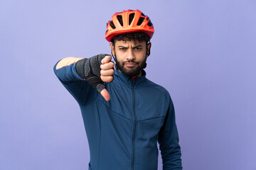 Young Moroccan cyclist man isolated on purple background showing thumb down with negative expression