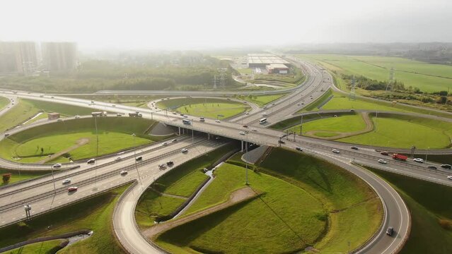 Highway multilevel traffic overpass intersection with driving automobiles among green meadows on city outskirts aerial panorama