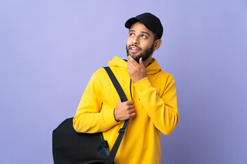 Young sport Moroccan man with sport bag isolated on purple background looking up while smiling
