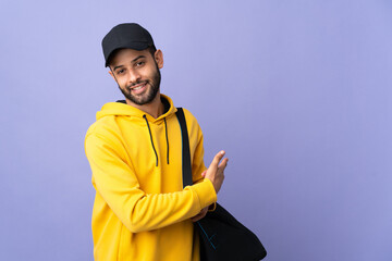 Young sport Moroccan man with sport bag isolated on purple background pointing back