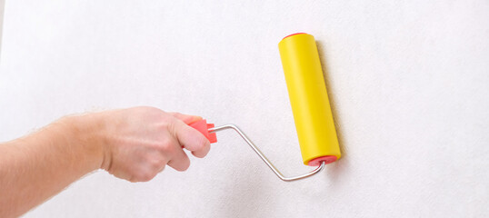 A man rolls out a canvas of white wallpaper with a suture yellow roller. Removing air bubbles and glue. Wallpapering. Repair of a room, apartment, house.