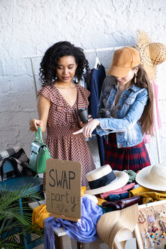 Happy women drinking coffee at swap party. Choose casual clothes, shoes, hats, bags, jewellery. Exchange your old wardrobe for new. Eco friendly cloth concept. Zero waste shopping, reduce and reuse