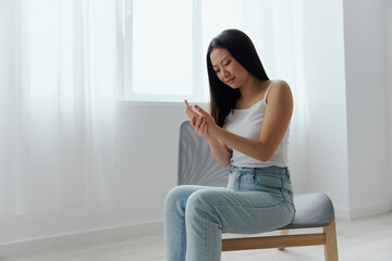 Broken hand Cramp. Upset suffering tanned beautiful young Asian woman touching massaging painful hand wrist at home interior living room. Injuries Poor health Illness concept. Cool offer Banner