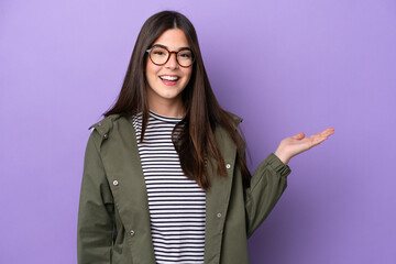 Young Brazilian woman isolated on purple background holding copyspace imaginary on the palm to...