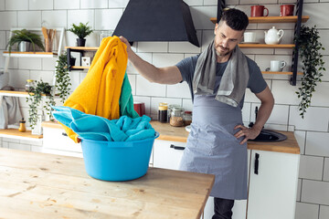 Handsome father, strong young man sorting laundry in the kitchen at home . Men doing chore