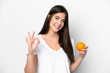 Young Brazilian woman holding an orange isolated on white background showing ok sign with fingers
