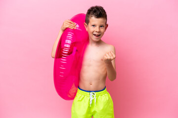 Little caucasian boy holding a inflatable donut isolated on pink background celebrating a victory in winner position © luismolinero