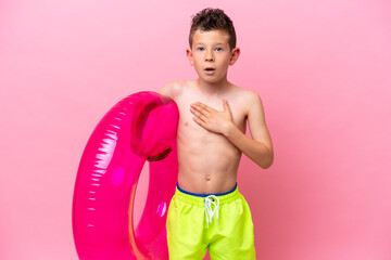 Little caucasian boy holding a inflatable donut isolated on pink background surprised and shocked...